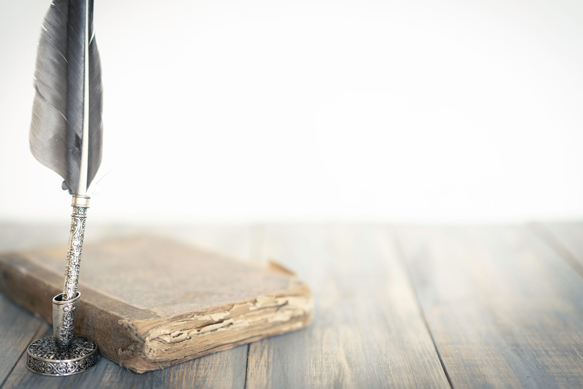 A quill pen and antique book on a writing desk