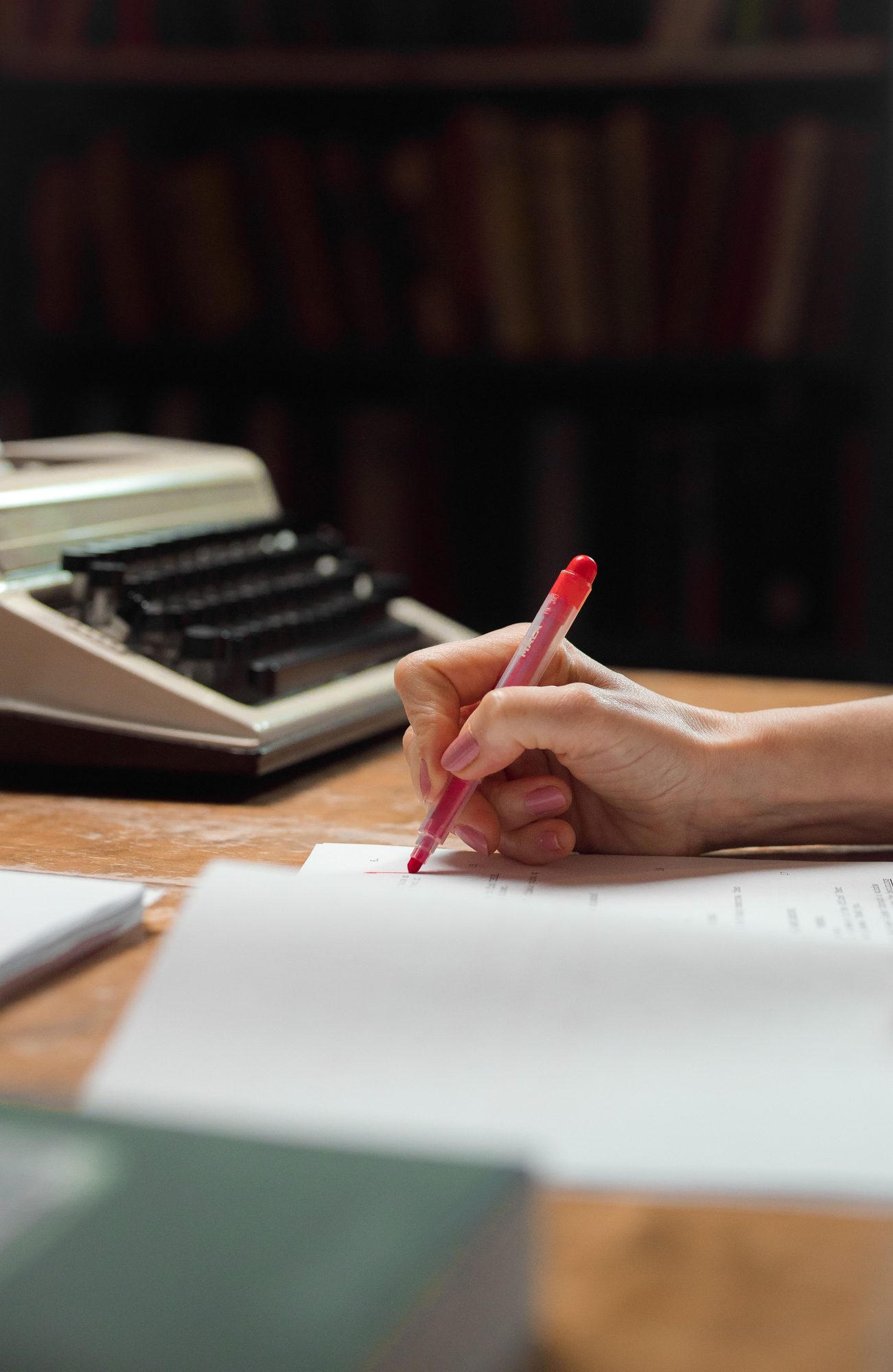 Hands revising a typed manuscript page with a red pen